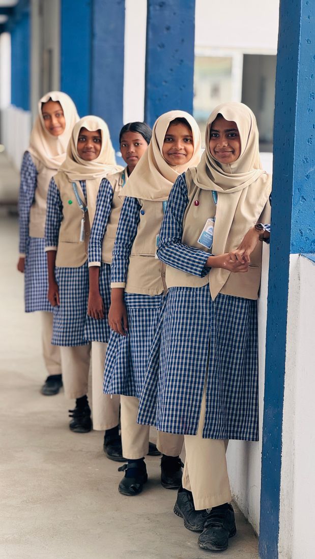 Five Markaz students in school uniform standing in a line along the blue and white corridor, smiling